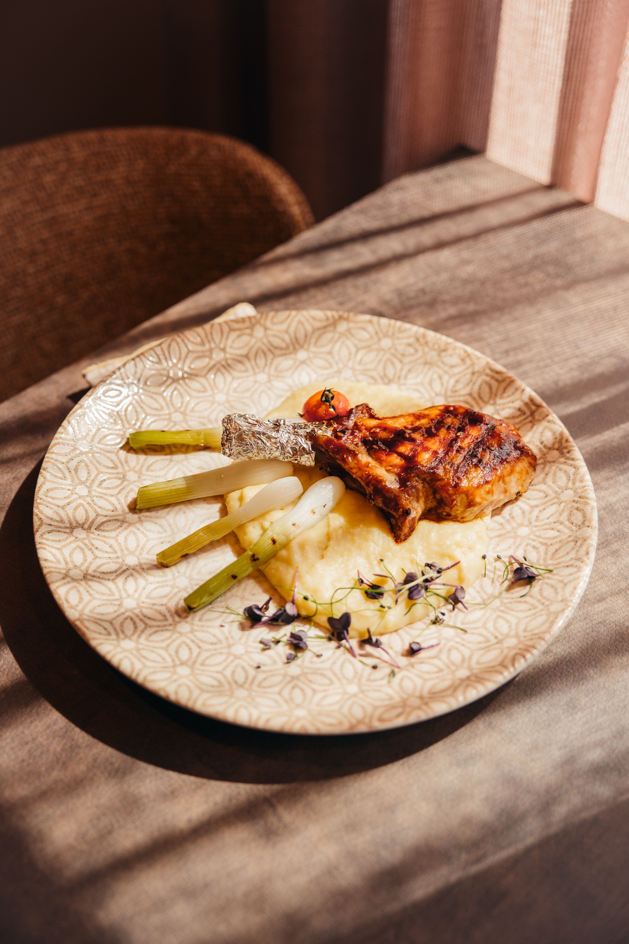 Gegrilltes Kotelett auf cremigem Püree mit Frühlingszwiebeln und Kresse im Streiflicht der Sonne