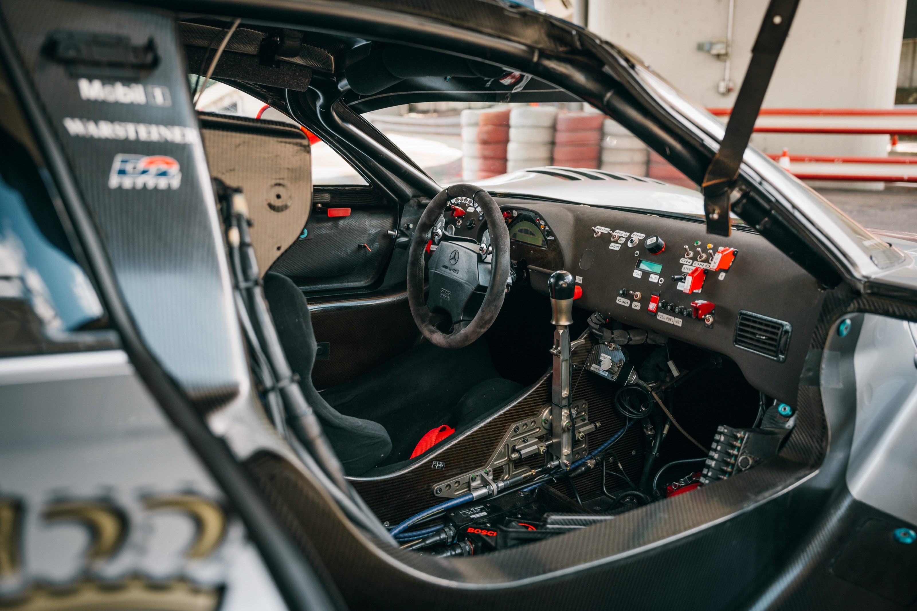 Cockpit des Rennwagens mit Überrollkäfig, Schalthebel und Schaltertafel hinter der geöffneten Tür