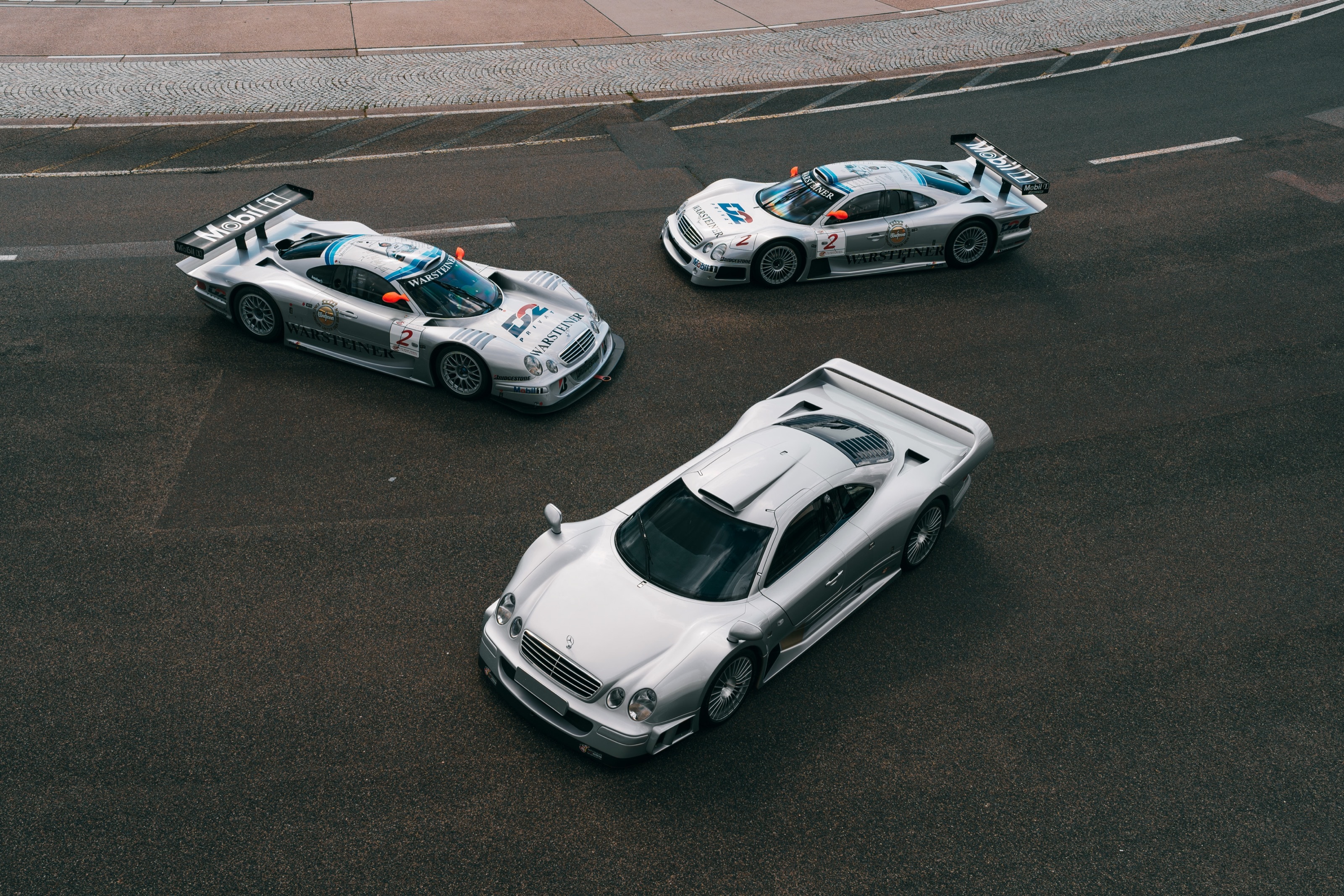 Straßenversion und zwei Rennwagen des CLK GTR von oben auf dunklem Asphalt