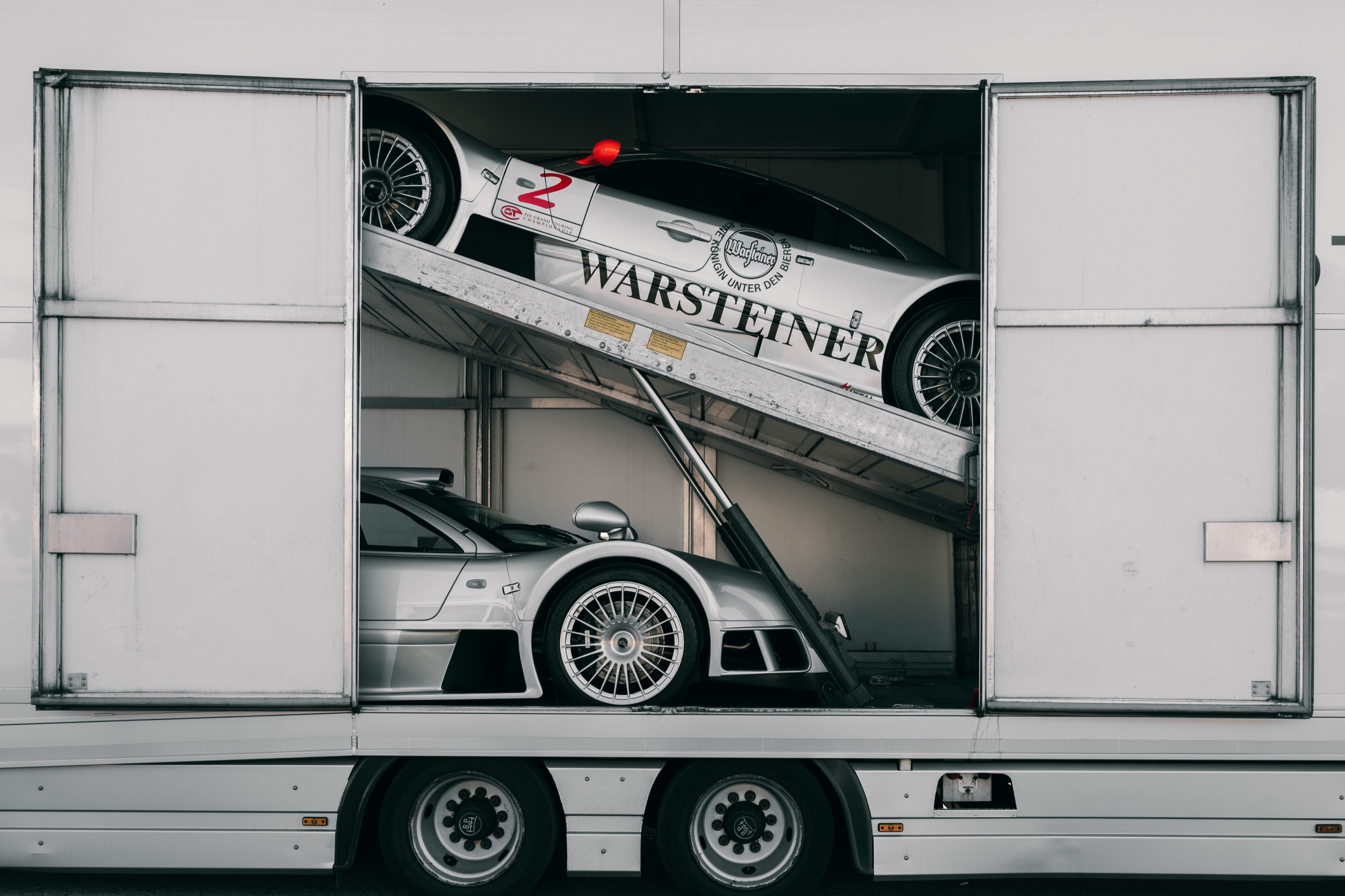 Rennwagen und Straßenversion übereinander im geöffneten Autotransporter