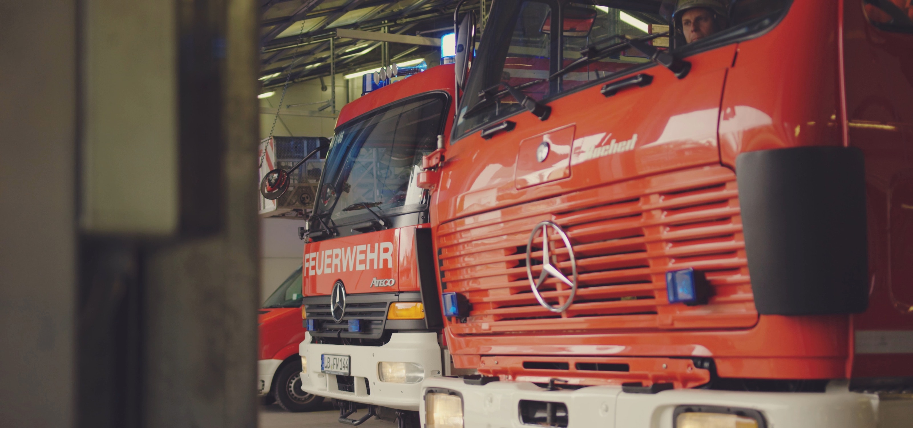Zwei Löschfahrzeuge in der Fahrzeughalle, hinter der Windschutzscheibe sitzt der Fahrer mit Helm