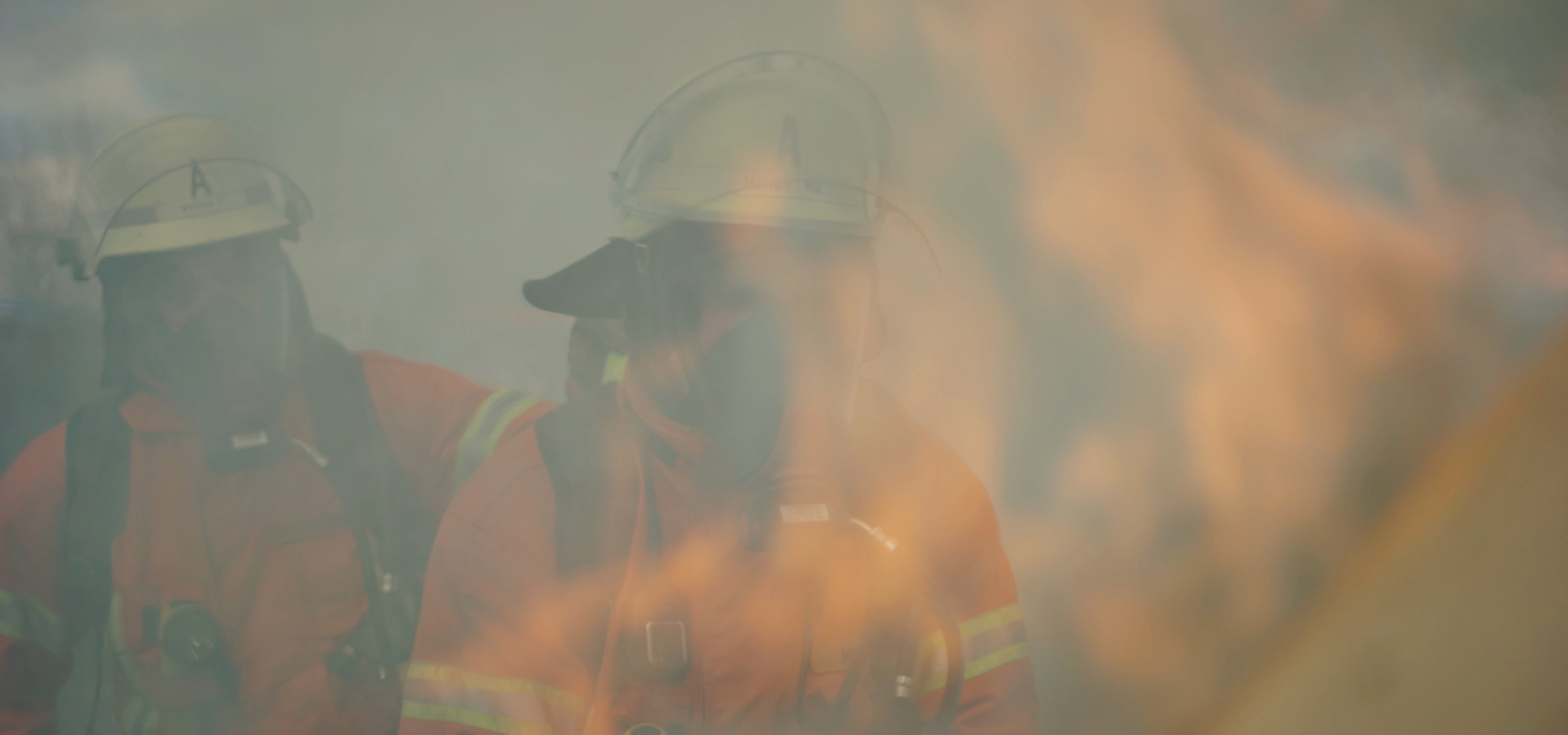 Zwei Einsatzkräfte mit Helm und Atemschutz hinter Flammen und Rauch