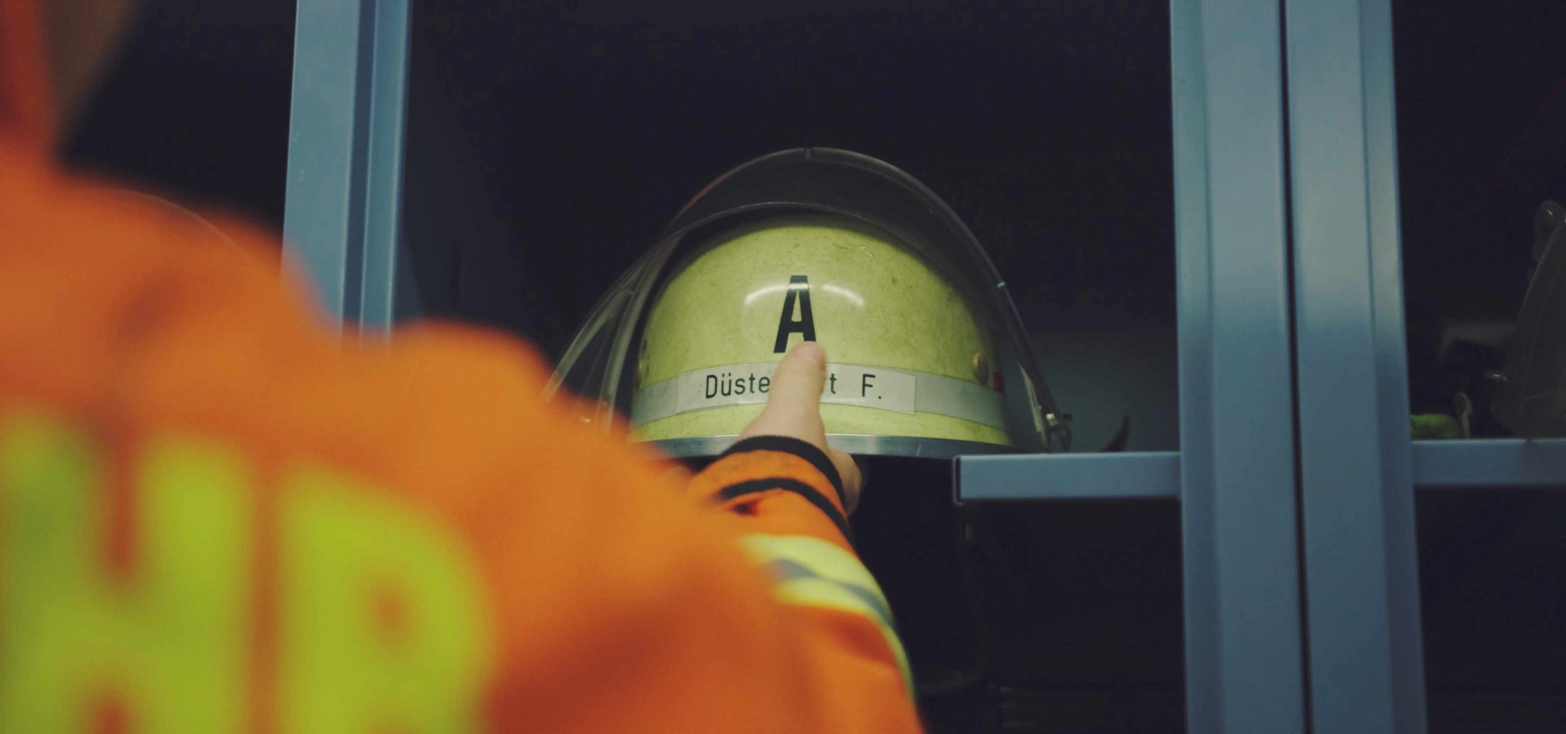 Eine Hand greift im Spind nach dem Feuerwehrhelm mit Visier