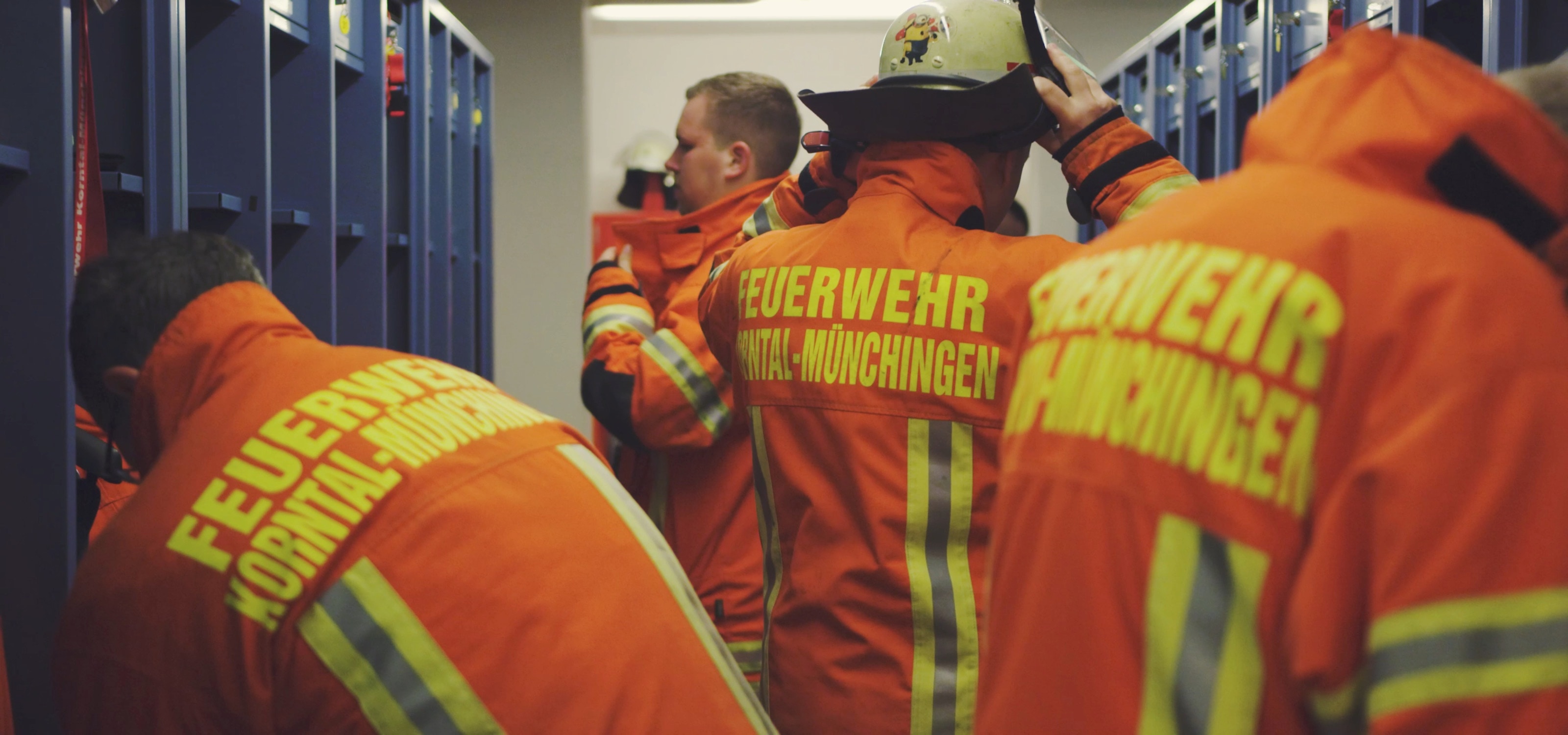 Einsatzkräfte ziehen in der Umkleide zwischen blauen Spinden ihre orangefarbenen Jacken mit der Aufschrift Feuerwehr Korntal-Münchingen an