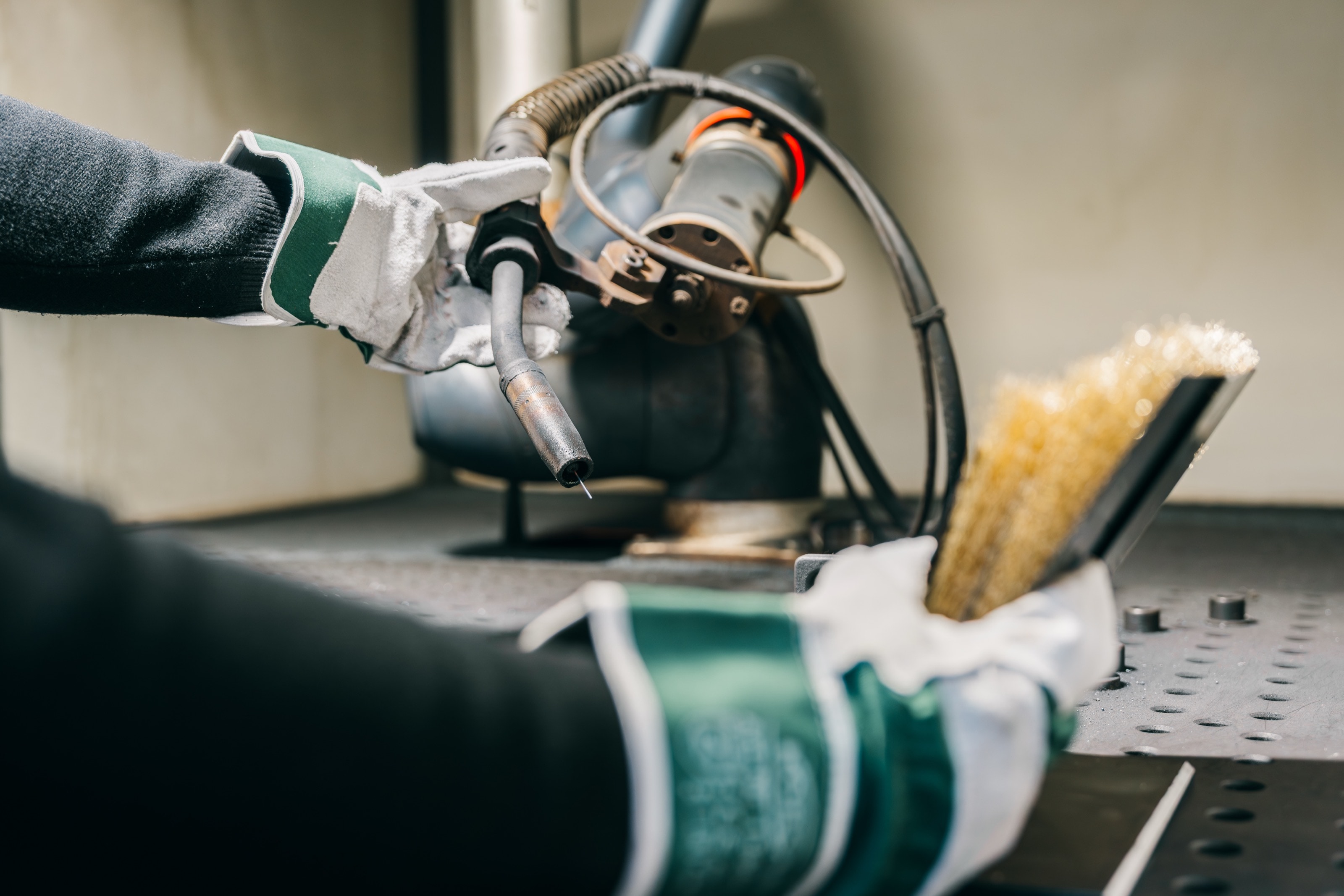 Hände in Schweißerhandschuhen reinigen den Schweißbrenner des Roboters mit einer Drahtbürste