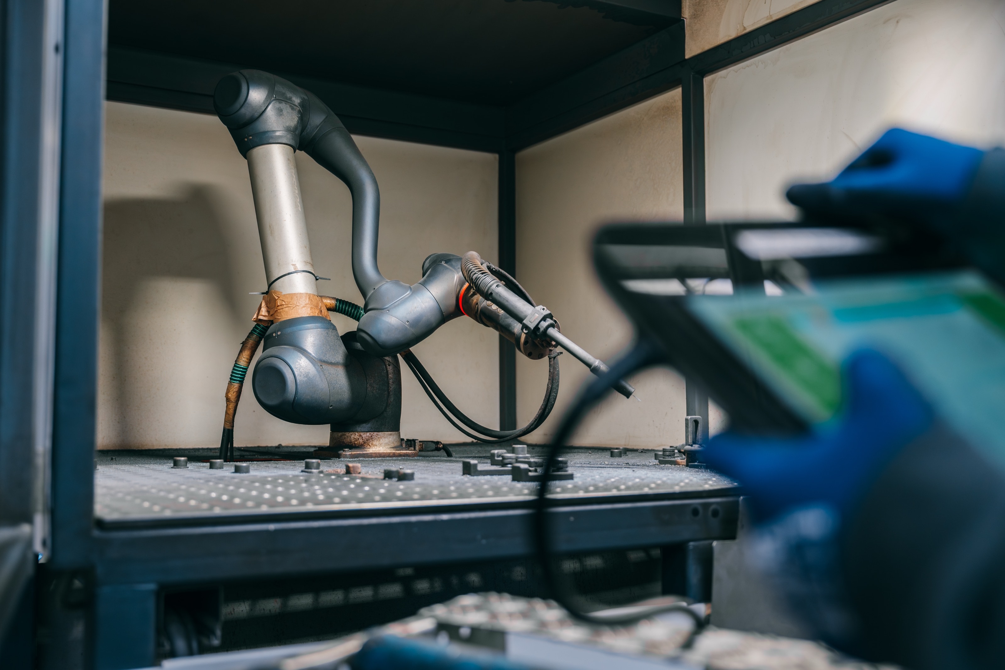 Kollaborierender Roboterarm mit Schweißbrenner, im Vordergrund ein Mitarbeiter mit Tablet
