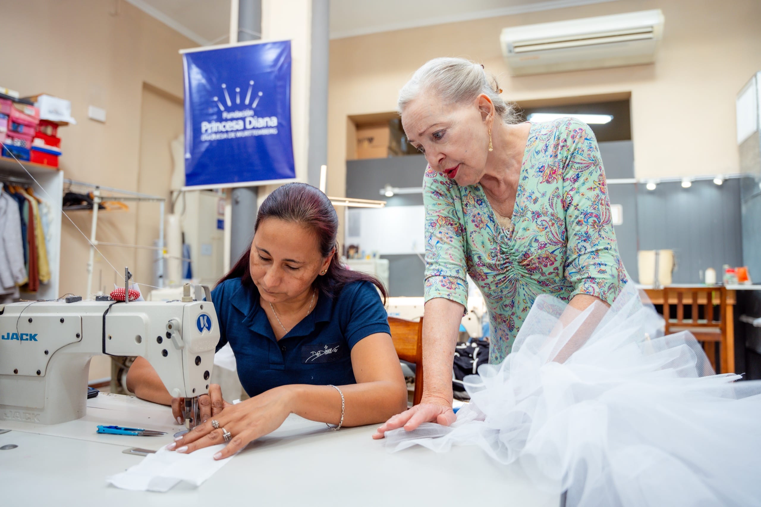 Näherin an der Industrienähmaschine im Atelier der Stiftung, angeleitet von einer Frau mit weißem Tüllstoff