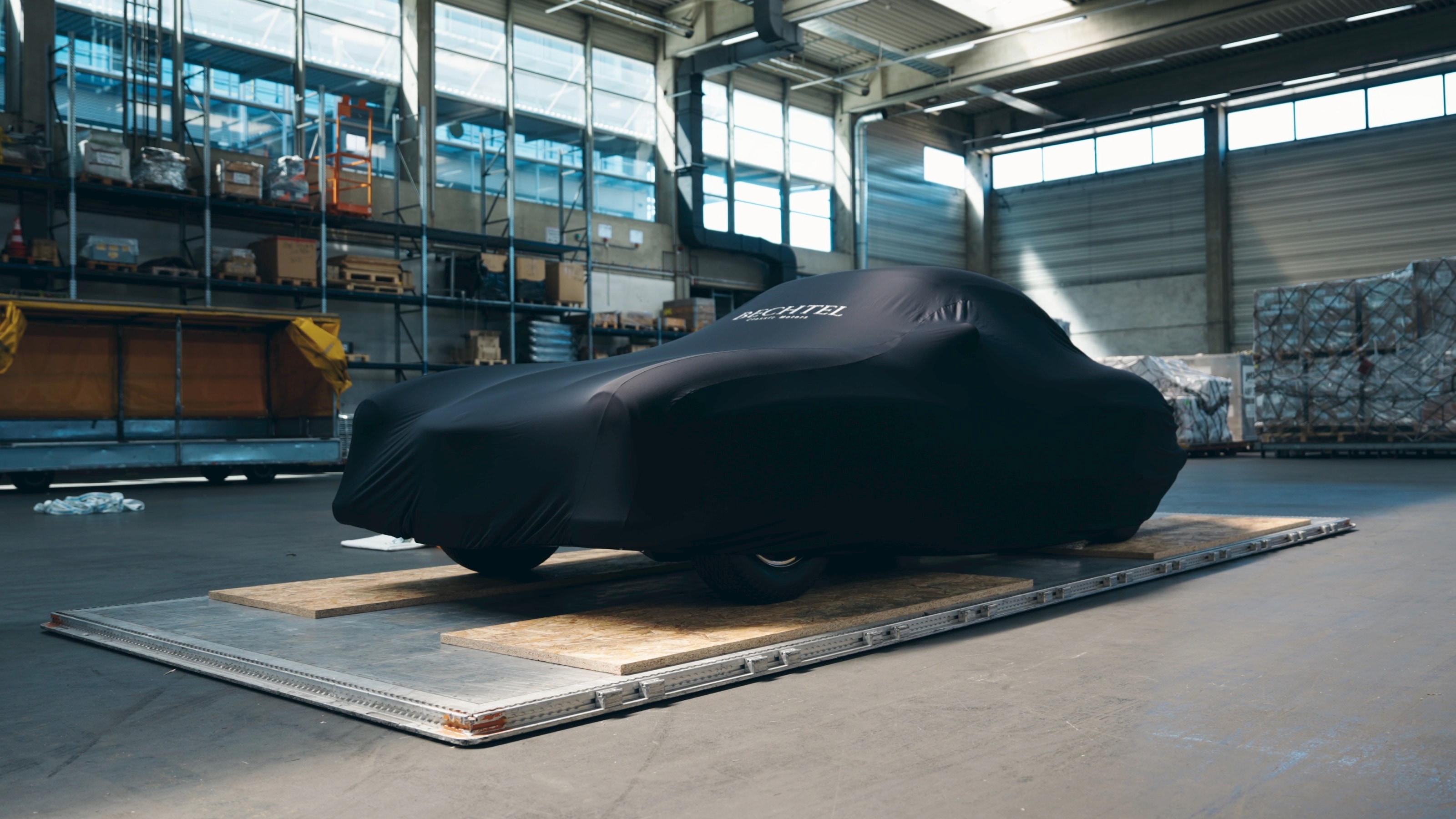 Der 300 SL unter einer schwarzen Bechtel-Abdeckplane auf einer Transportpalette in einer Lagerhalle