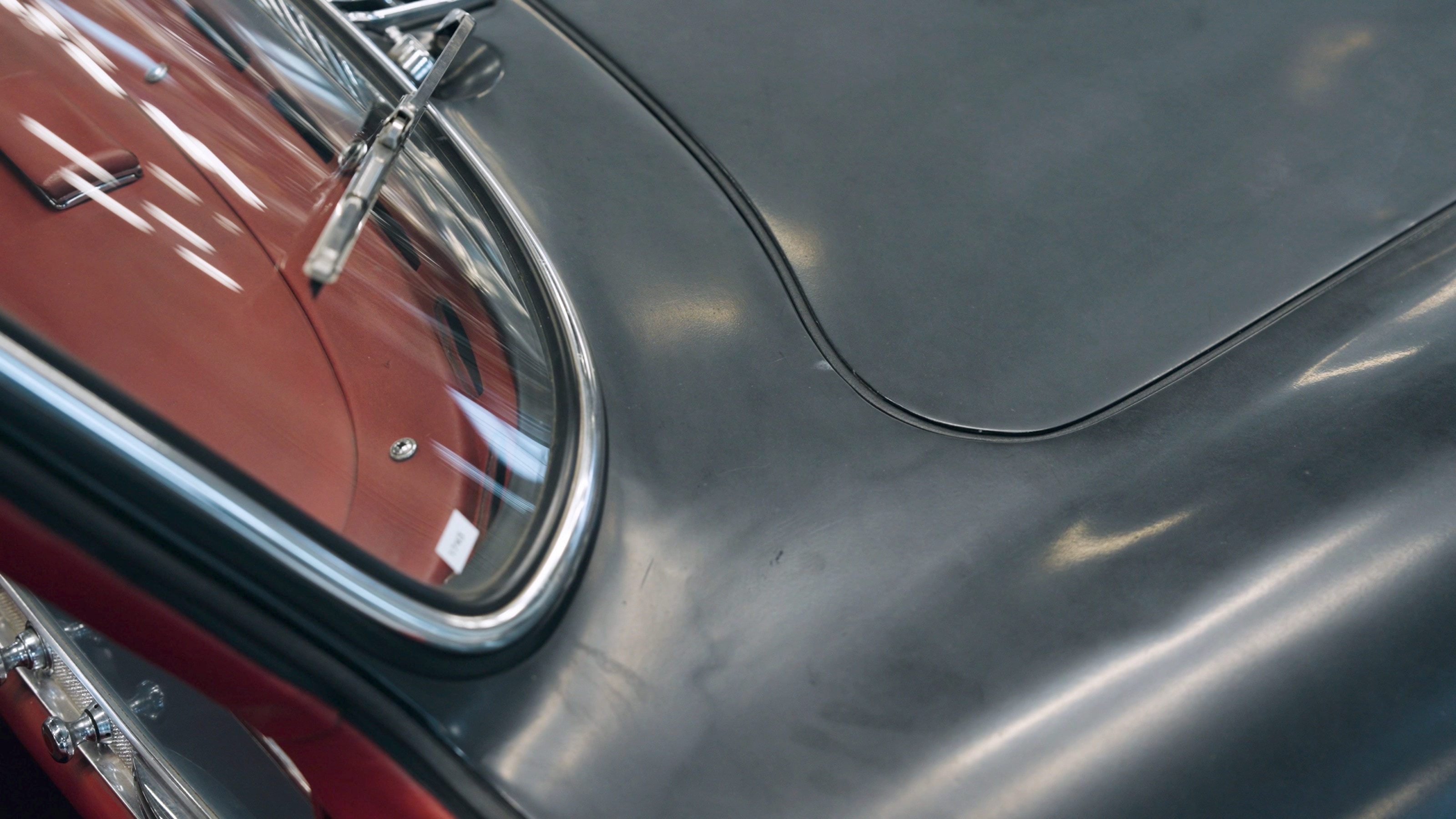 Detail der anthrazitfarbenen Motorhaube und des Kotflügels am Rand der Frontscheibe, dahinter das rote Armaturenbrett