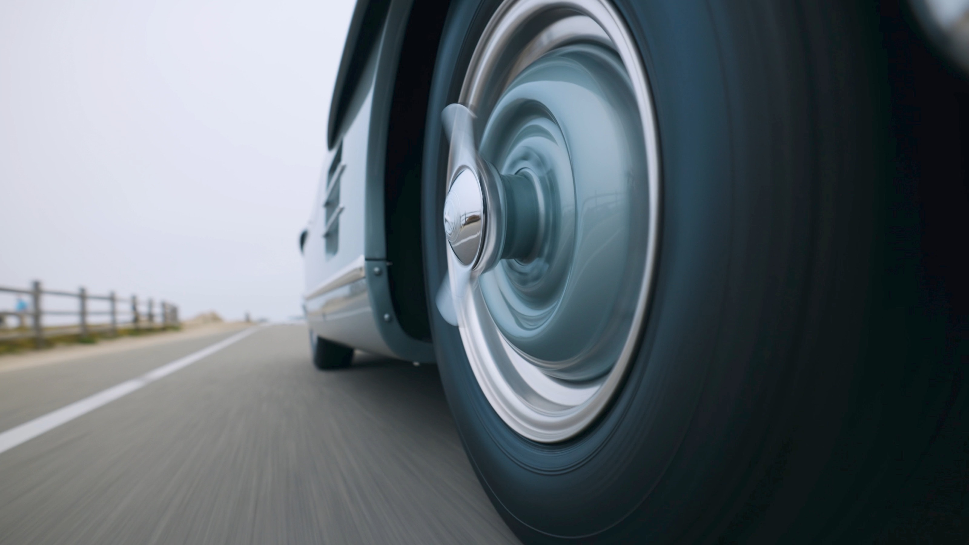 Tiefe Kamerafahrt am Vorderrad des 300 SL mit Chromradkappe auf einer nebligen Küstenstraße