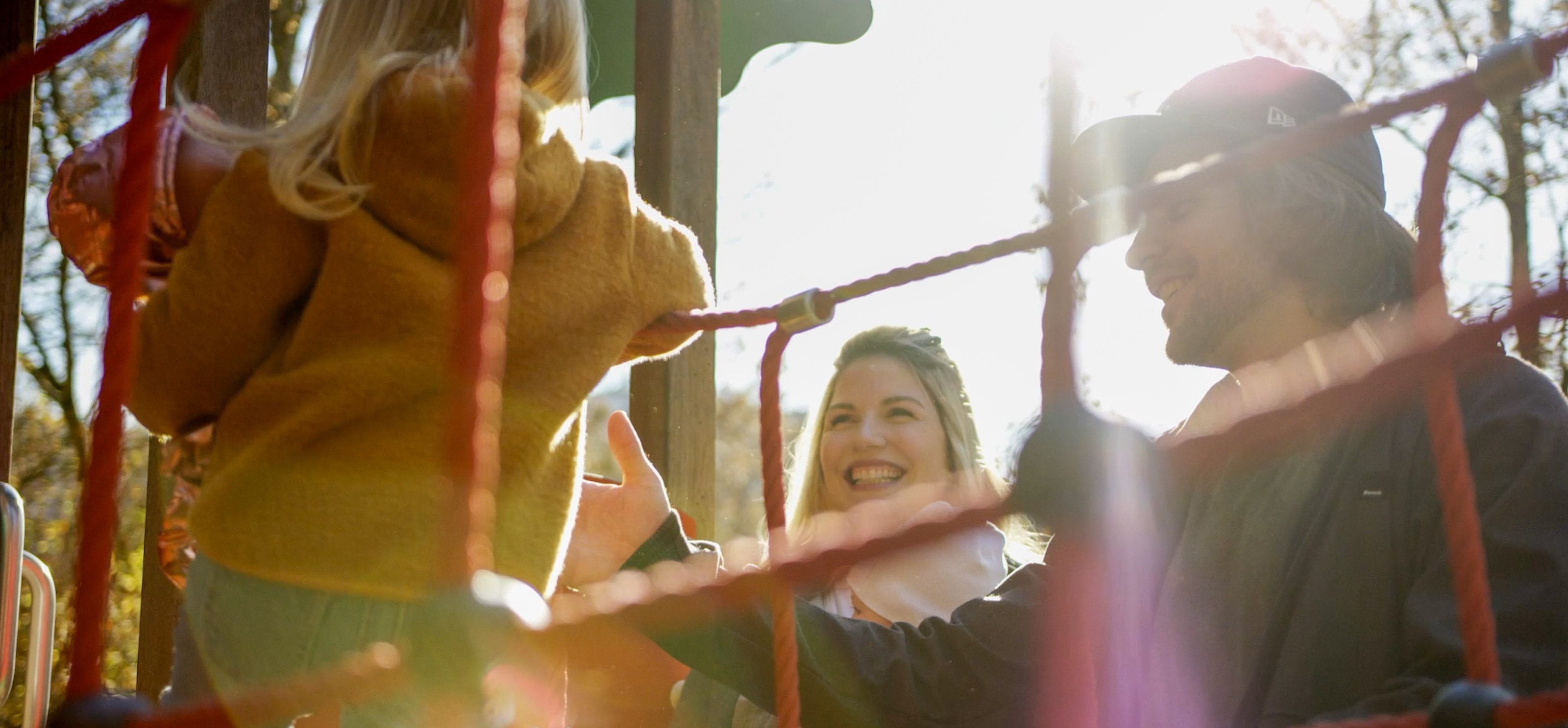Familie auf dem roten Klettergerüst eines Spielplatzes, im Gegenlicht der Herbstsonne