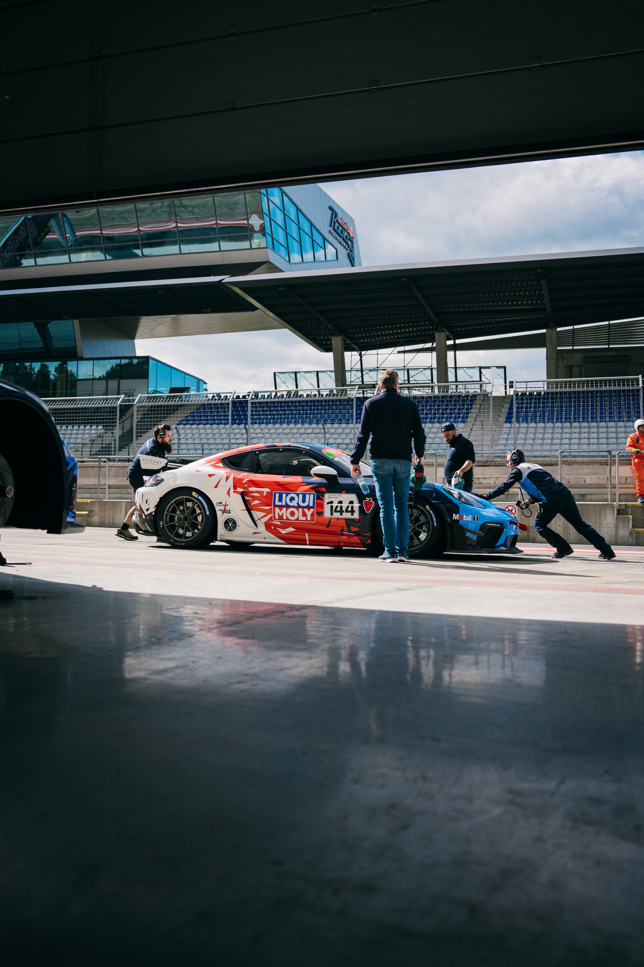 Blick aus der Box auf den 911 GT3 Cup in der spiegelnden Boxengasse, daneben ein Mechaniker