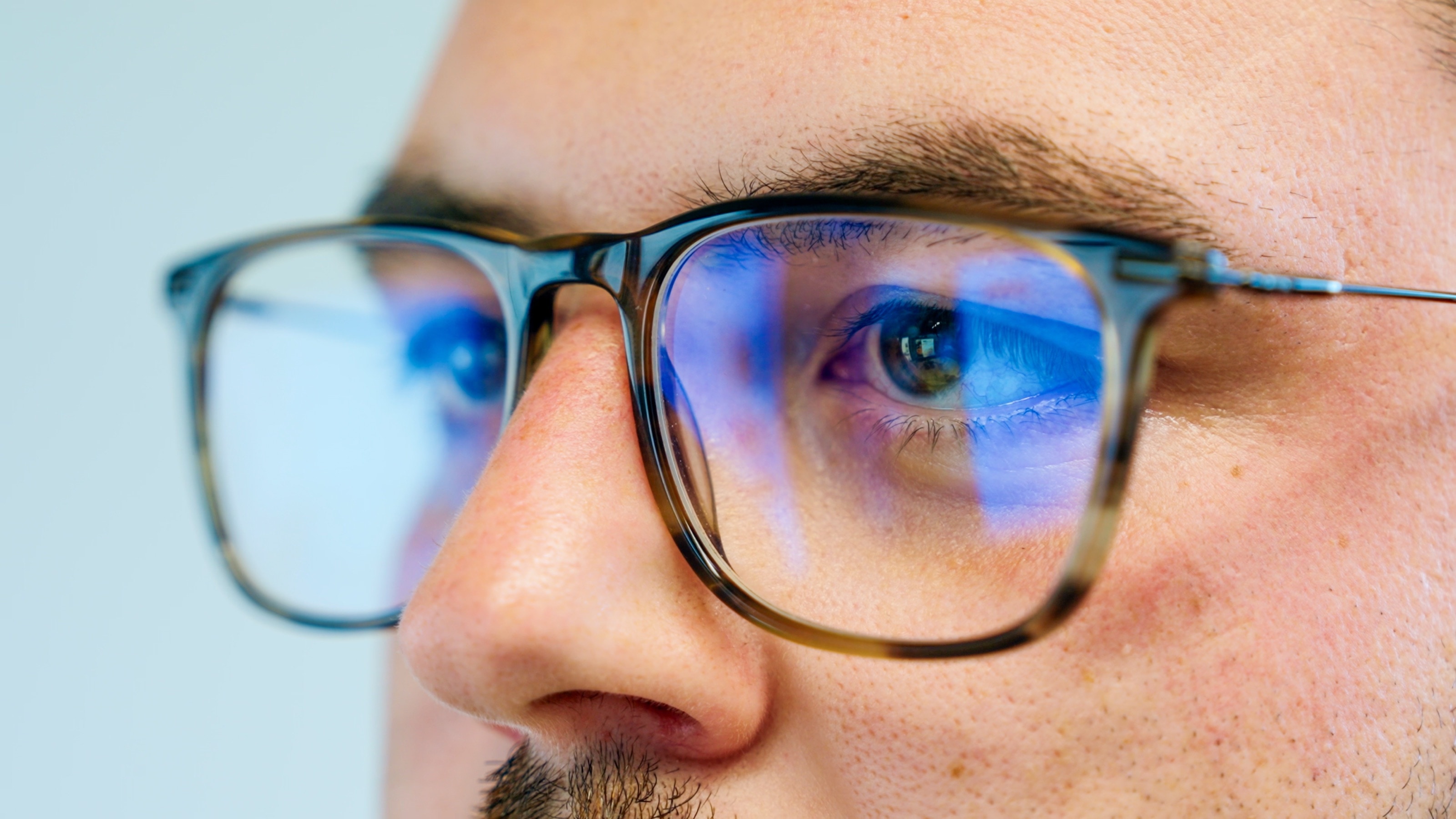 Nahaufnahme eines Auges hinter einer Hornbrille, im Brillenglas spiegelt sich blaues Bildschirmlicht