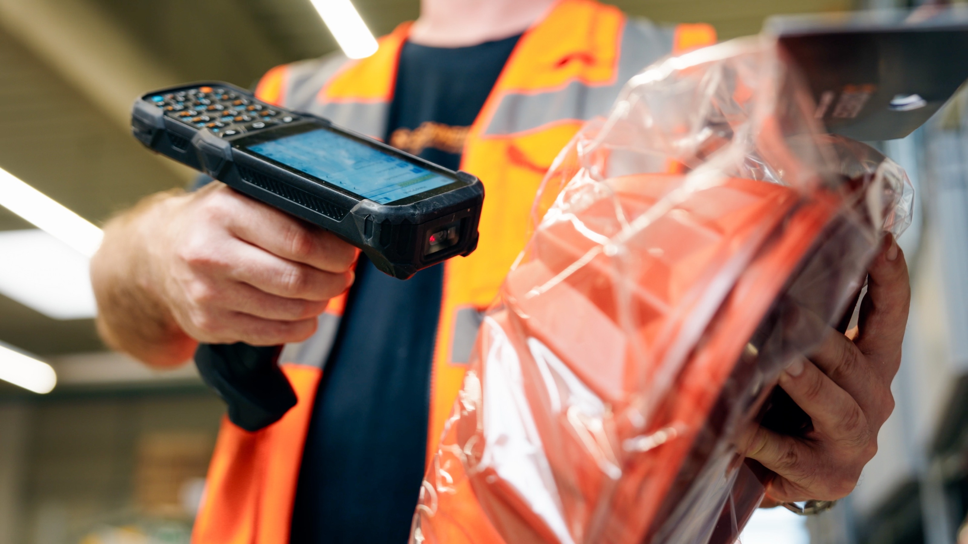 Mitarbeiter in Warnweste scannt bei der Kommissionierung einen in Folie verpackten Artikel mit dem Handscanner