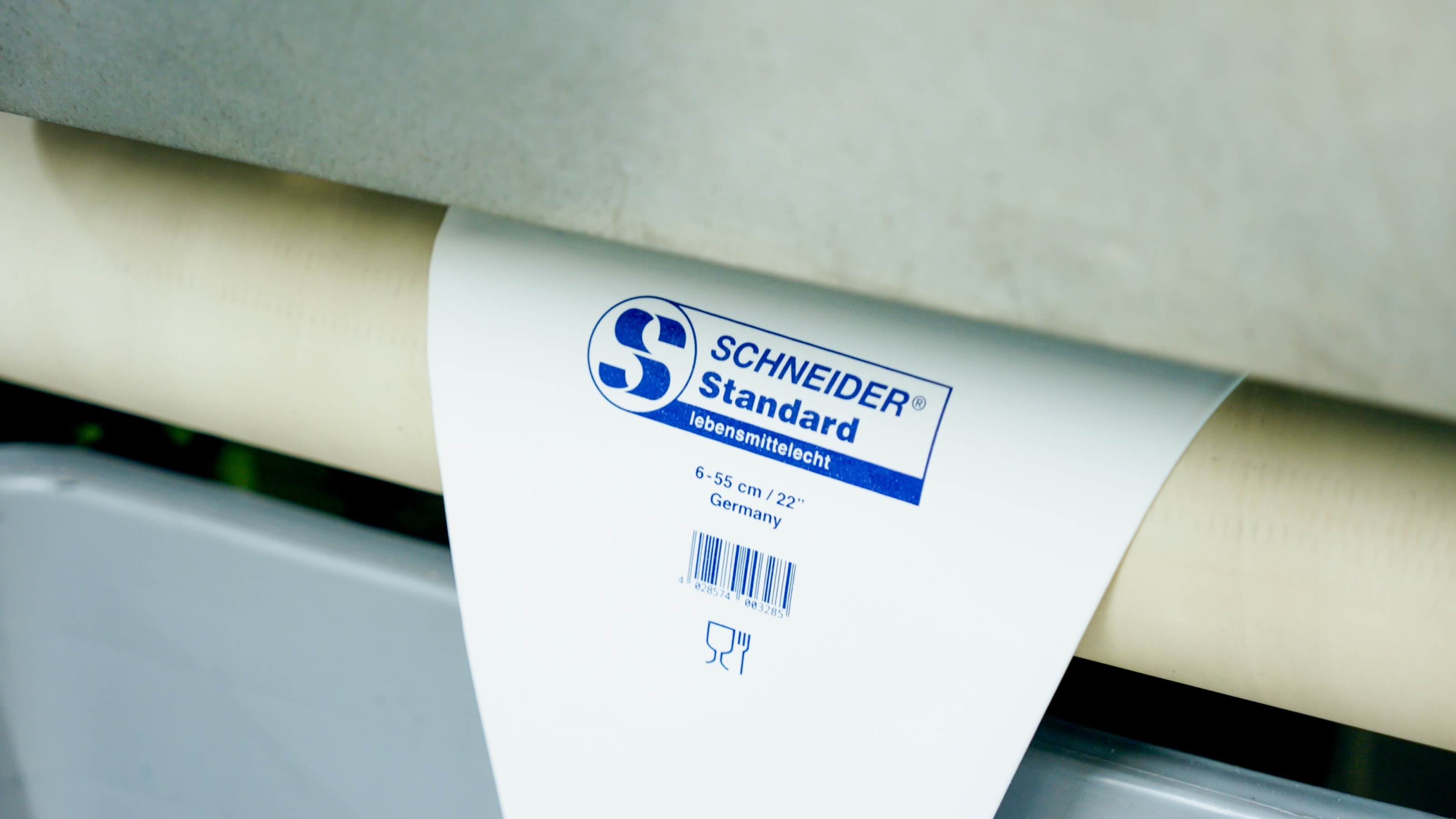 Bedruckter Spritzbeutel mit dem Aufdruck „Schneider Standard – lebensmittelecht“ hängt über einer Walze