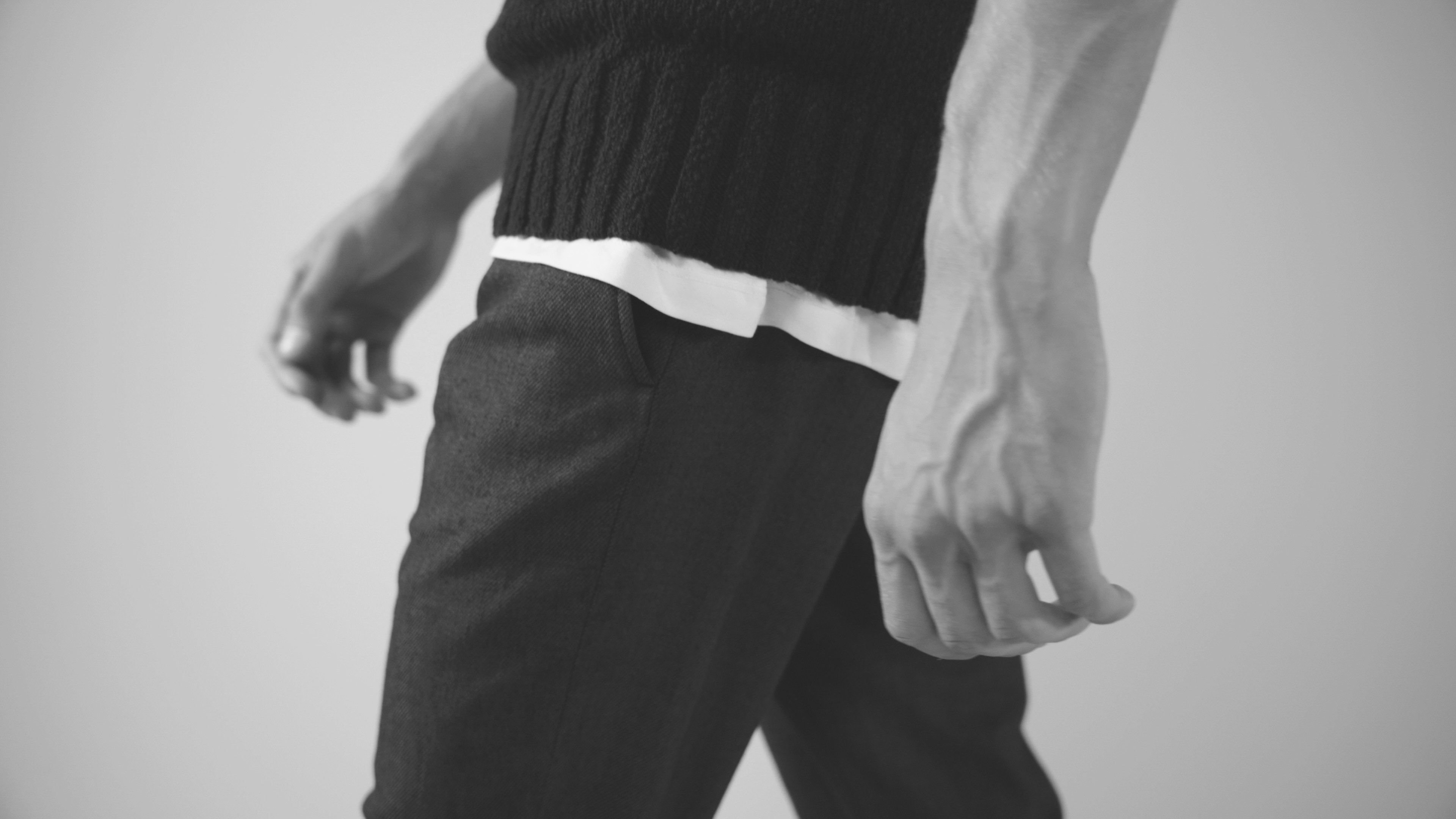 Model in Strickpullunder und dunkler Hose in der Bewegung, Detail von Hose und Händen
