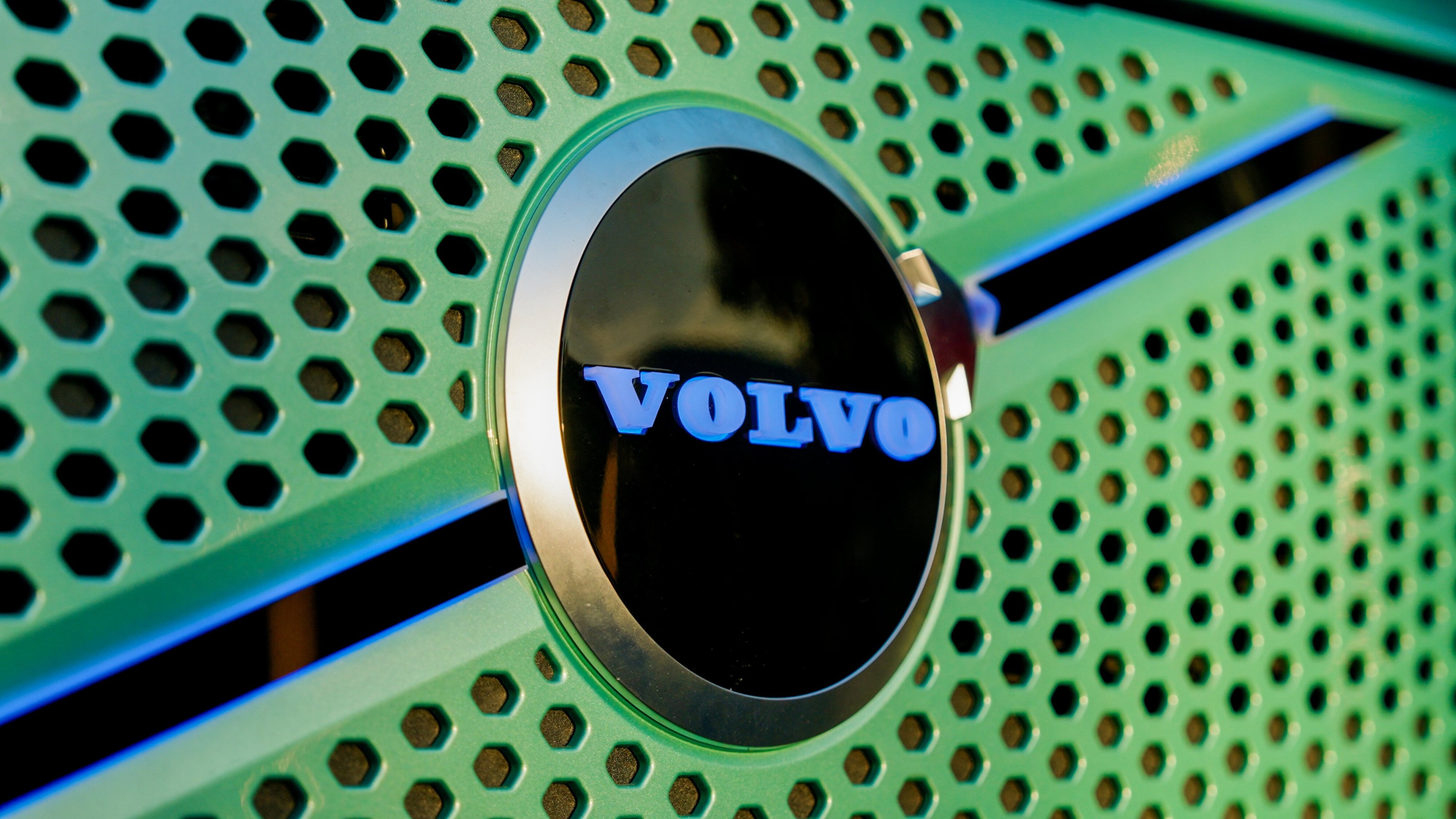 Nahaufnahme des Volvo-Emblems im wabenförmig perforierten Kühlergrill der grün folierten Front