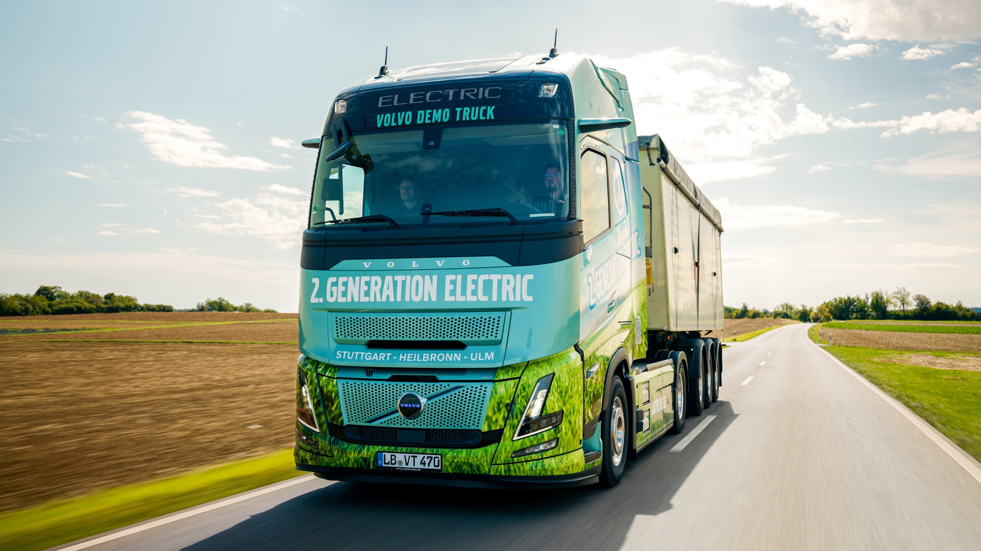 Der Volvo FH Aero Electric im Gegenlicht auf einer Landstraße, die sich zwischen Feldern in die Ferne zieht