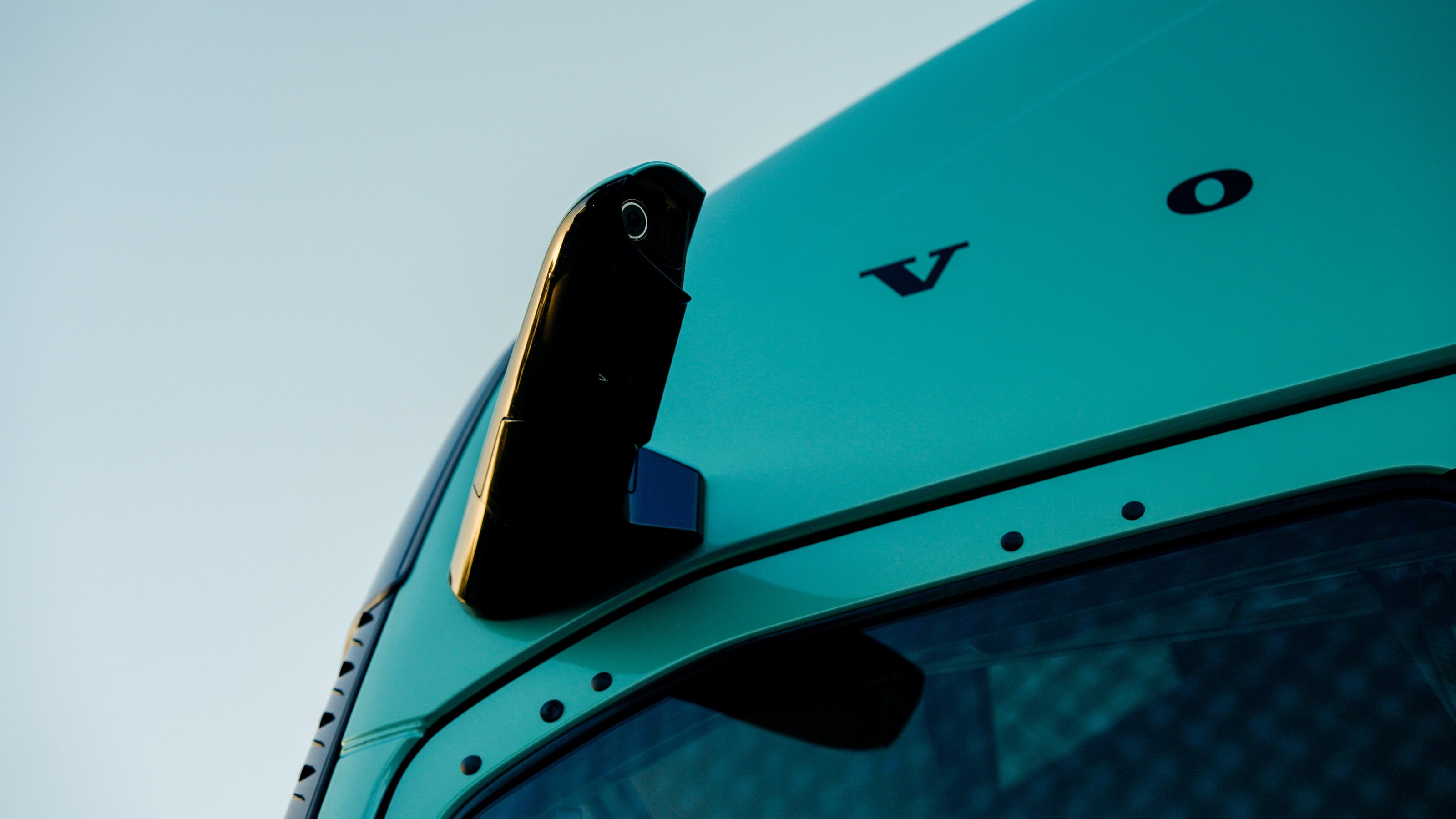 Der Kamera-Arm des Spiegelersatzsystems und der Volvo-Schriftzug am türkisen Fahrerhaus vor hellem Himmel